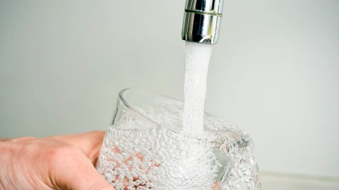 en person fylder et glas med vand fra vandhanen