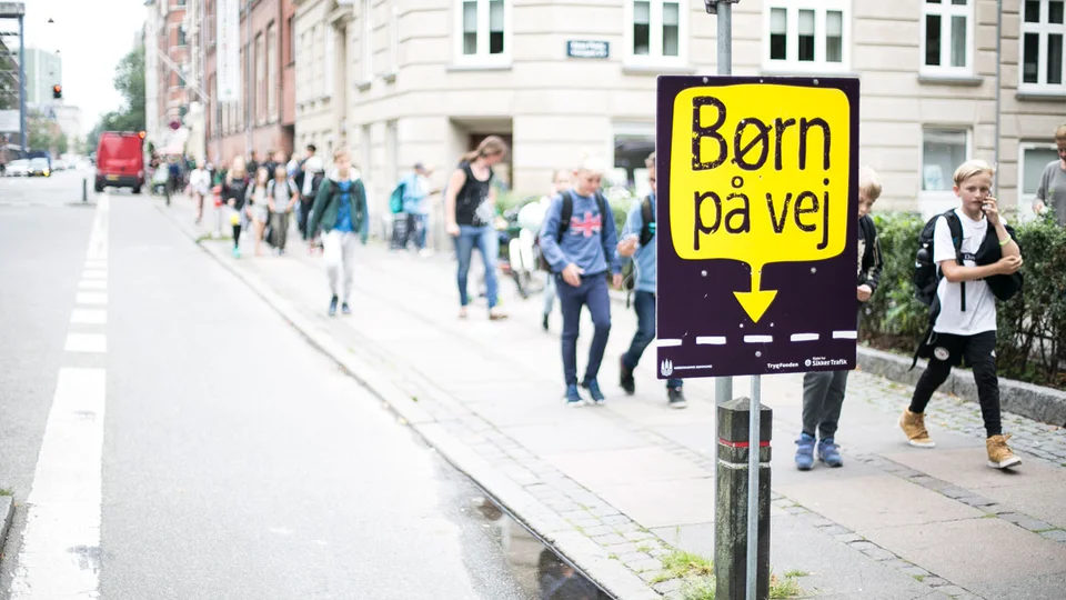 Børn på vej i skole med en plakat fra Rådet for Sikker Trafik i forgrunden - Børn på vej