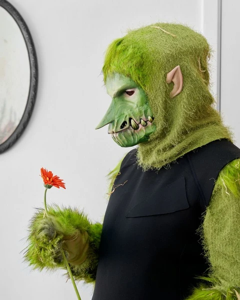 Portræt af kunstner med grøn maske og orange blomst.