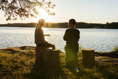 To mennesker, der sidder på træstubbe i modlys ved vandkanten
