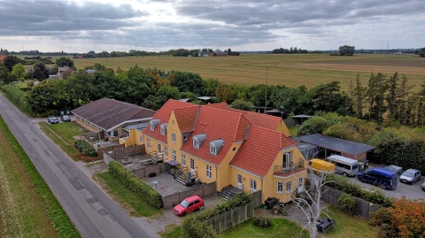 En gammel landejendom i to etager. Der er to indhegnede gårdhaver ud for bygningen. 