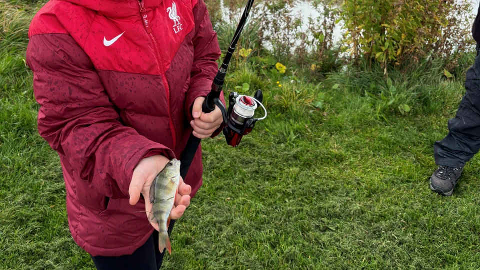 Barn med fiskestang og en fisk i hånden