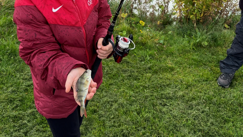 Barn med fiskestang og en fisk i hånden