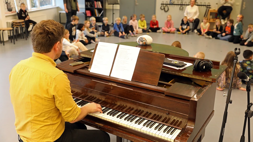Skolebørn øver sange med en pianist ved et klaver