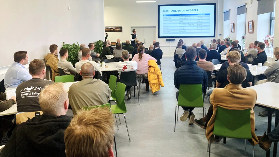 Billede af mennesker i en sal, der sidder ved borde og ser en præsentation