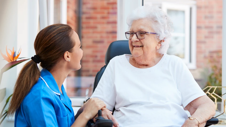 Plejer taler med ældre kvinde i rullestol